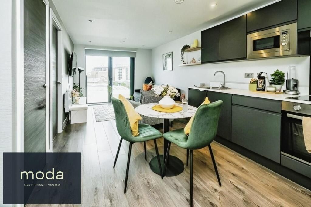 Modern apartment interior with kitchen, dining area, and living space. Green chairs, marble table, and dark cabinets.