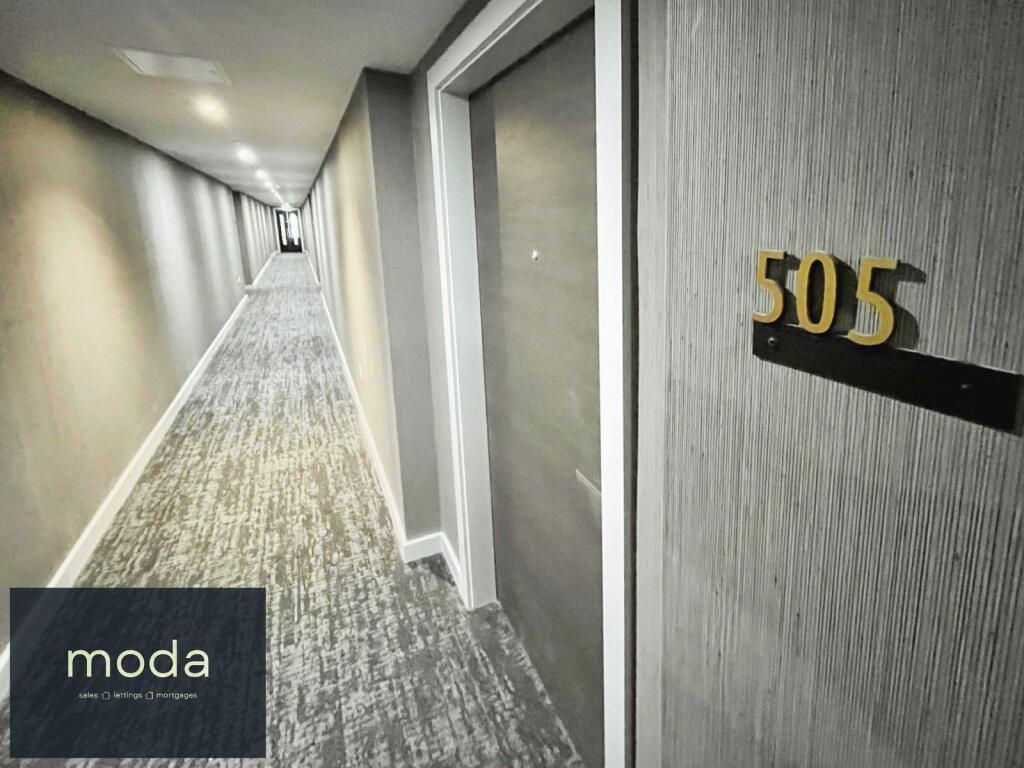 A long, modern hotel hallway with room 505. Gray walls, patterned carpet, and a door with gold numbers.