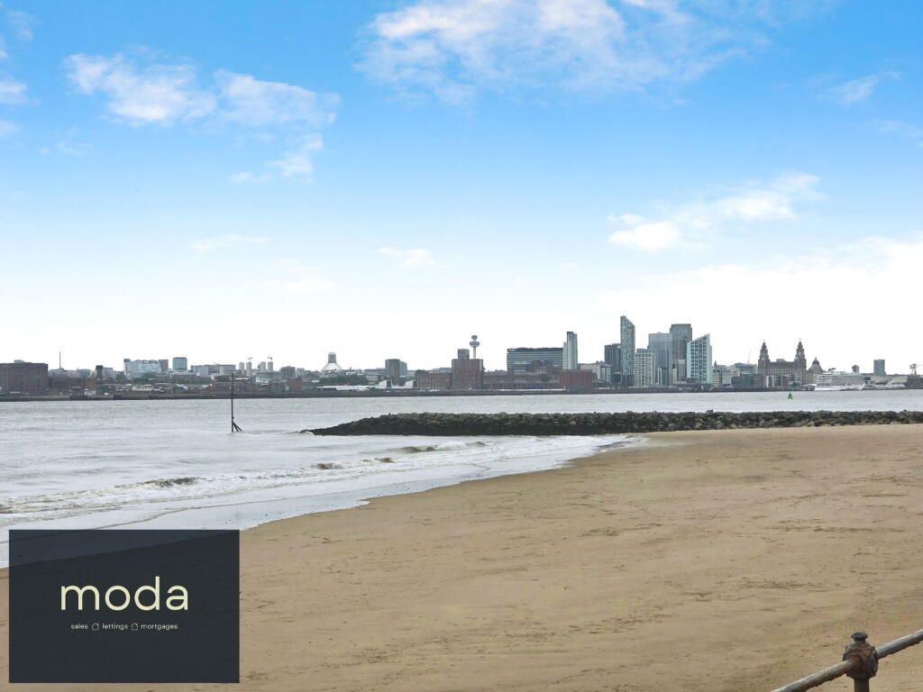 Sandy beach with city skyline across the water under a blue sky.