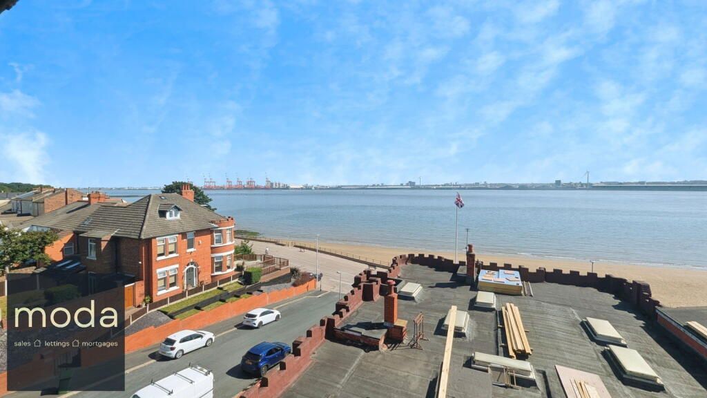 View of a coastal area with a beach, buildings, road, water, and blue sky.