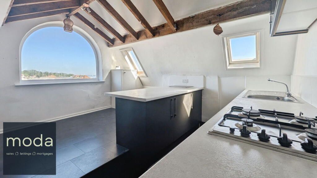 Kitchen with arched window, white countertops, dark cabinets, and exposed beams.