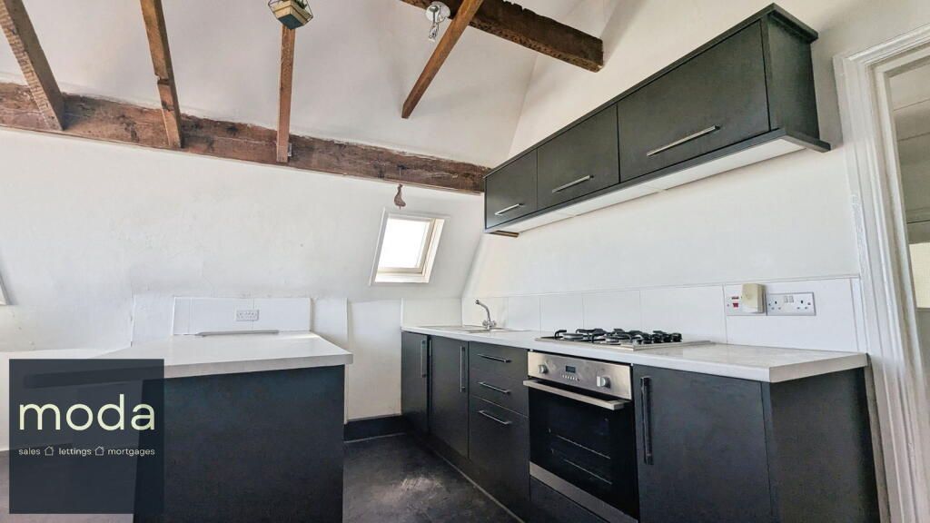 Kitchen with black cabinets, white countertops, and exposed wooden beams in a slanted ceiling.