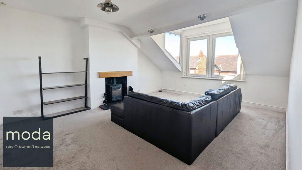 Spacious, angled-ceiling living room with a dark sectional sofa, fireplace, and window.