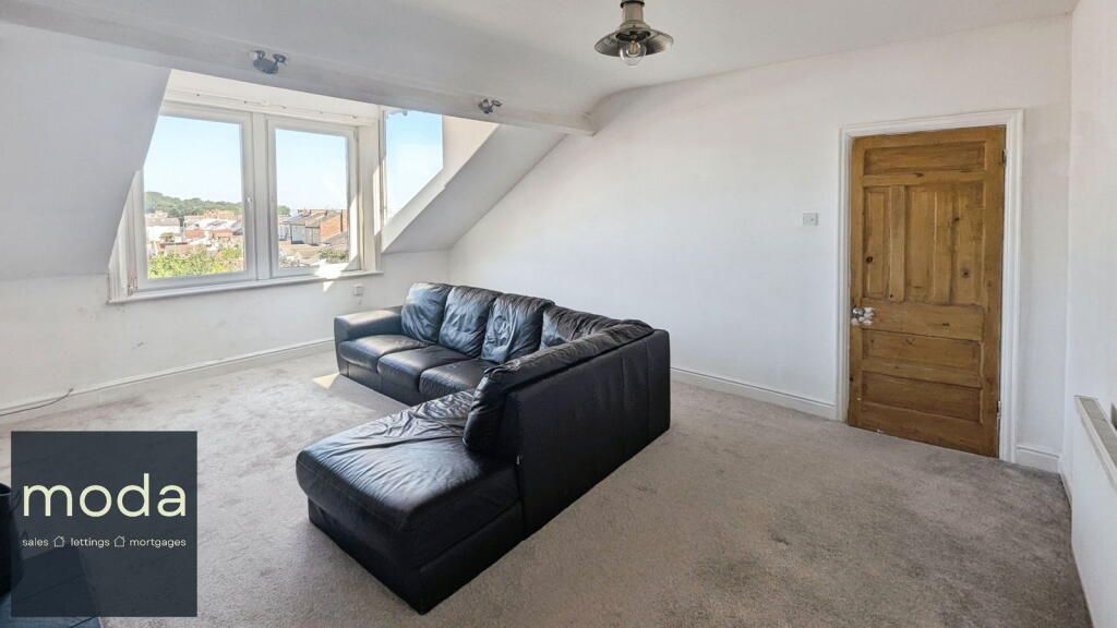 A living room with a black leather sectional, window, and light-colored walls and carpet.