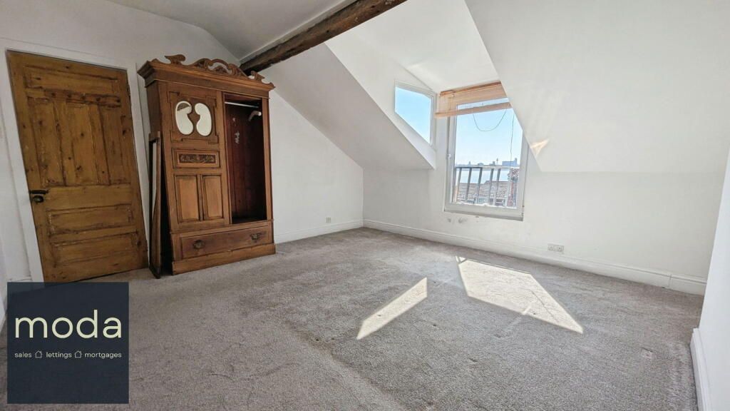 Attic bedroom with slanted walls, wooden wardrobe, and window. Gray carpet, light walls.
