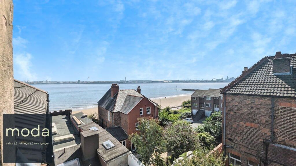 View of a sandy beach, houses, and cityscape under a bright blue sky.