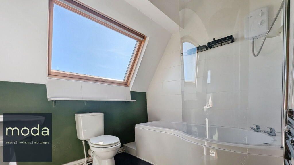 Bathroom with skylight, green wall, white toilet, tub, and shower curtain.