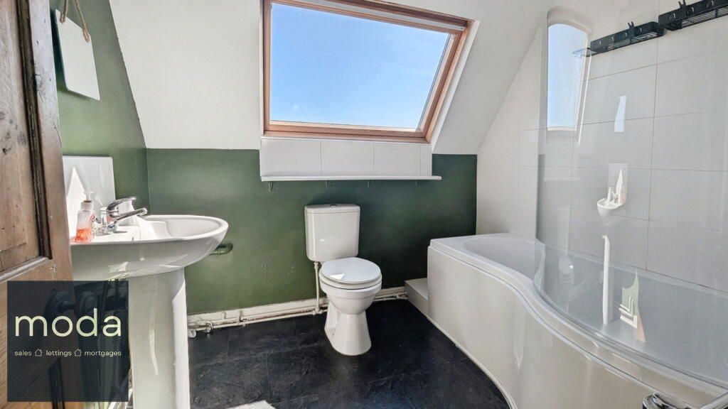 Bathroom with dark floor, toilet, sink, bathtub, and skylight. Walls are white and green.