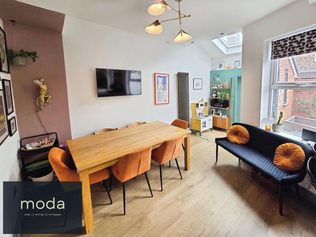 Dining area with wooden table and orange chairs, black sofa with orange pillows, skylight, and wall-mounted TV.