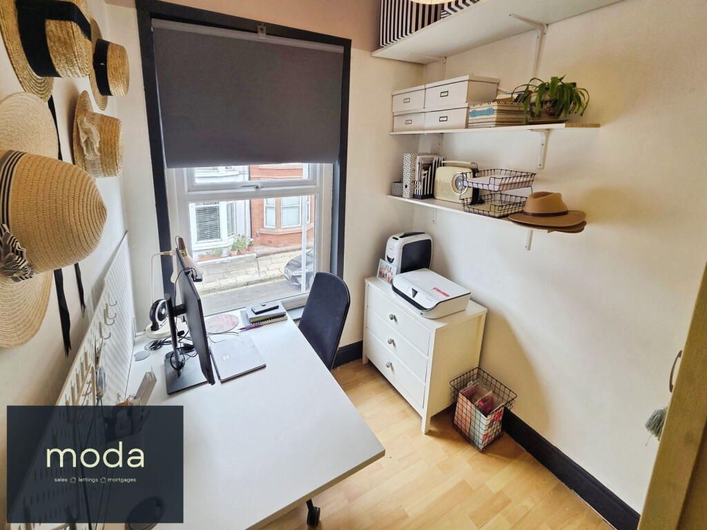 Office space with desk, window, shelves, and a chest of drawers. Decorated with hats and plants.