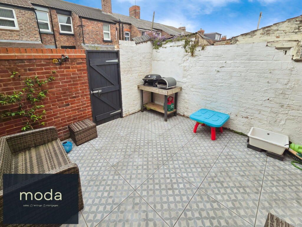 Small outdoor patio with tiled floor, brick and white walls, wooden table and grill.