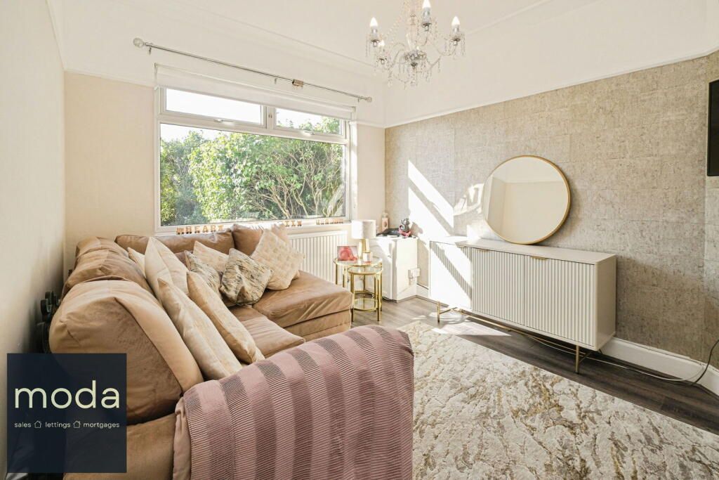 A cozy living room with a large window, beige sofa, and decorative mirror.