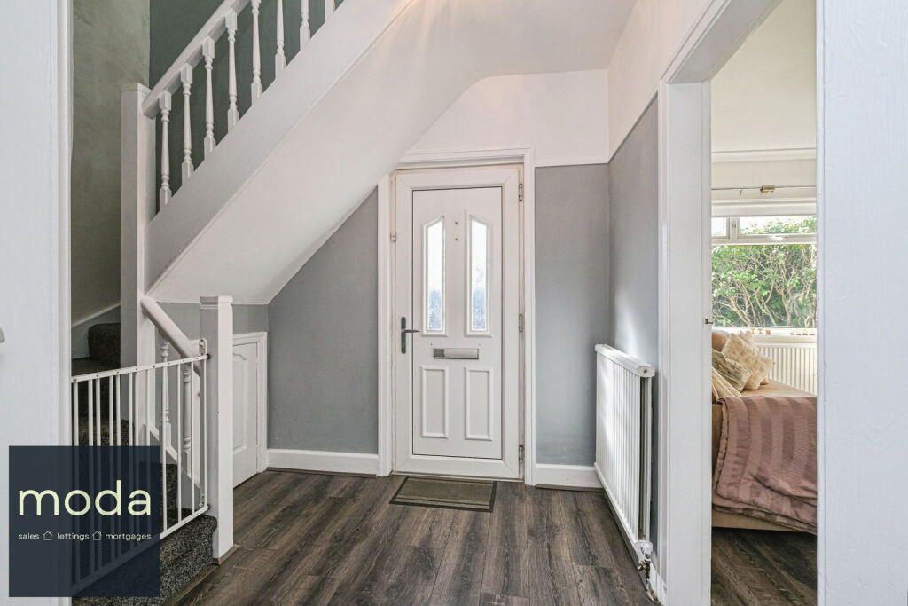 Hallway with staircase, white door, gray walls, wood-look flooring, and view into a bedroom.