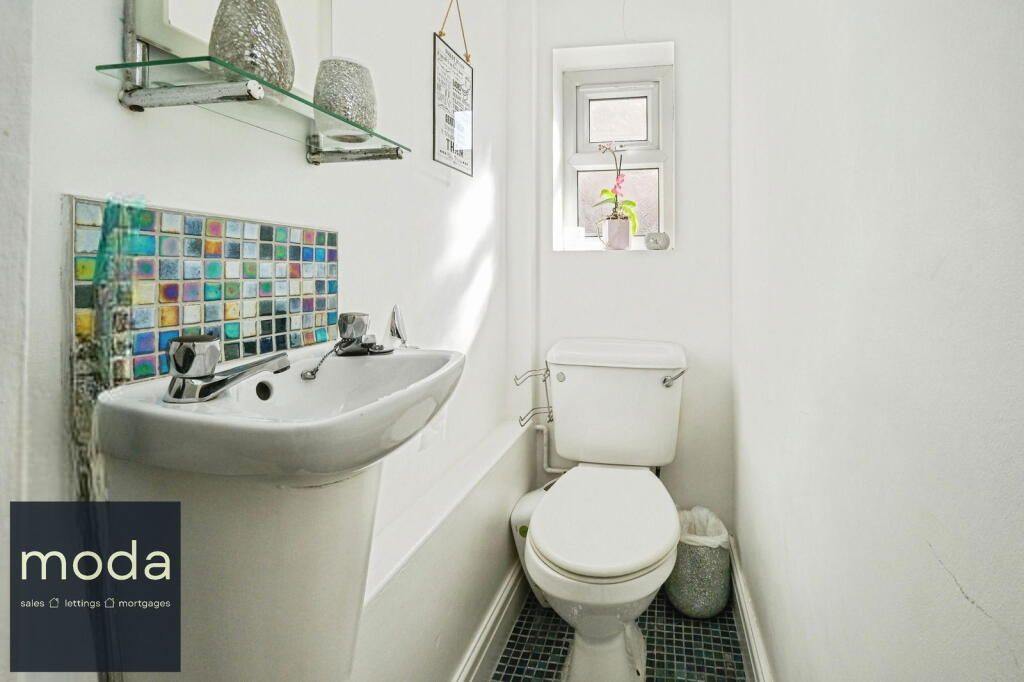 Small white bathroom with a toilet, sink, and colorful tiled backsplash.