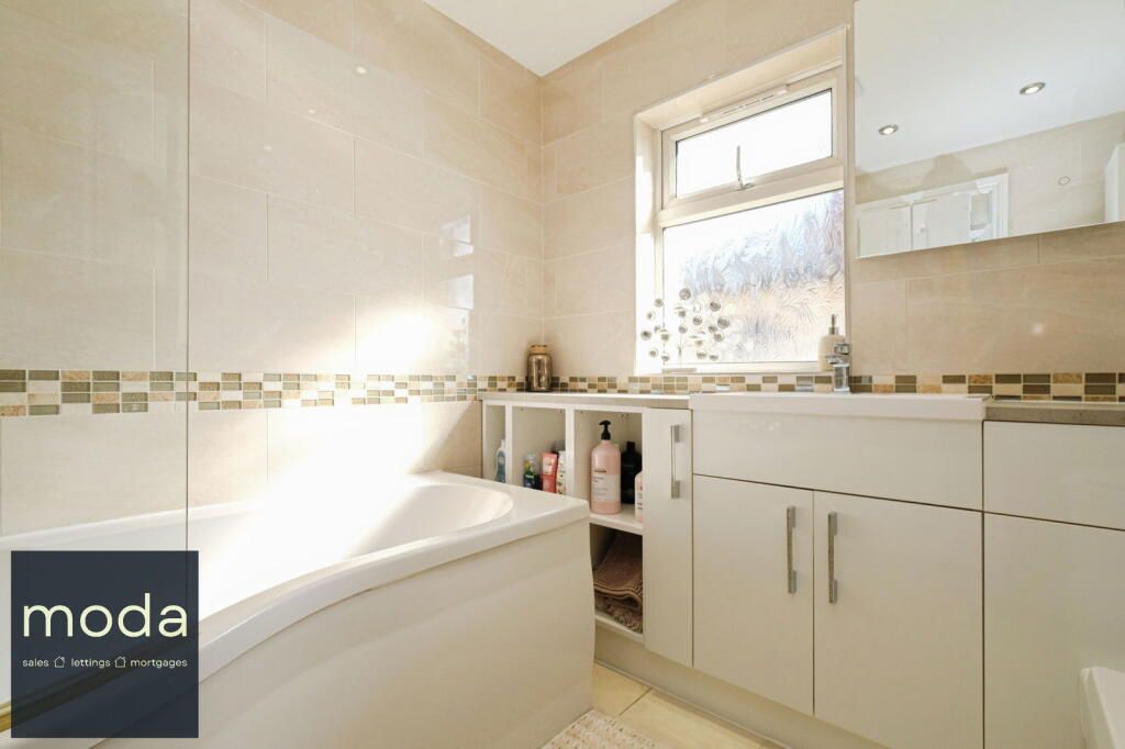 Bathroom with bathtub, sink, and cabinets. Light beige and white tiles.