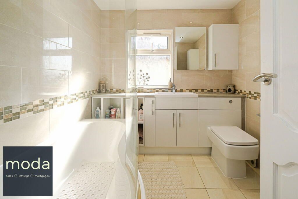 Bathroom with a bathtub, toilet, sink, cabinets, and a window with beige and white tiles.