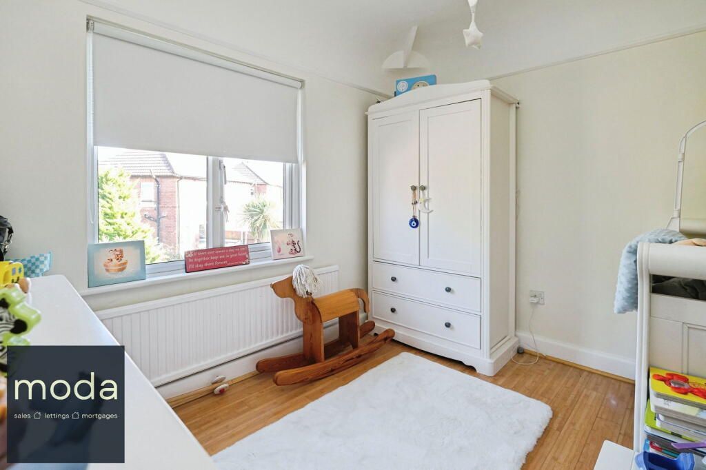 A bright child's bedroom with white walls, a window, wardrobe, rocking horse, and white rug.