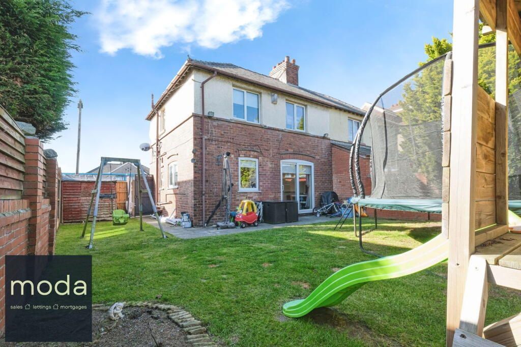 Rear view of a two-story house with a trampoline and a green slide in the grassy backyard.