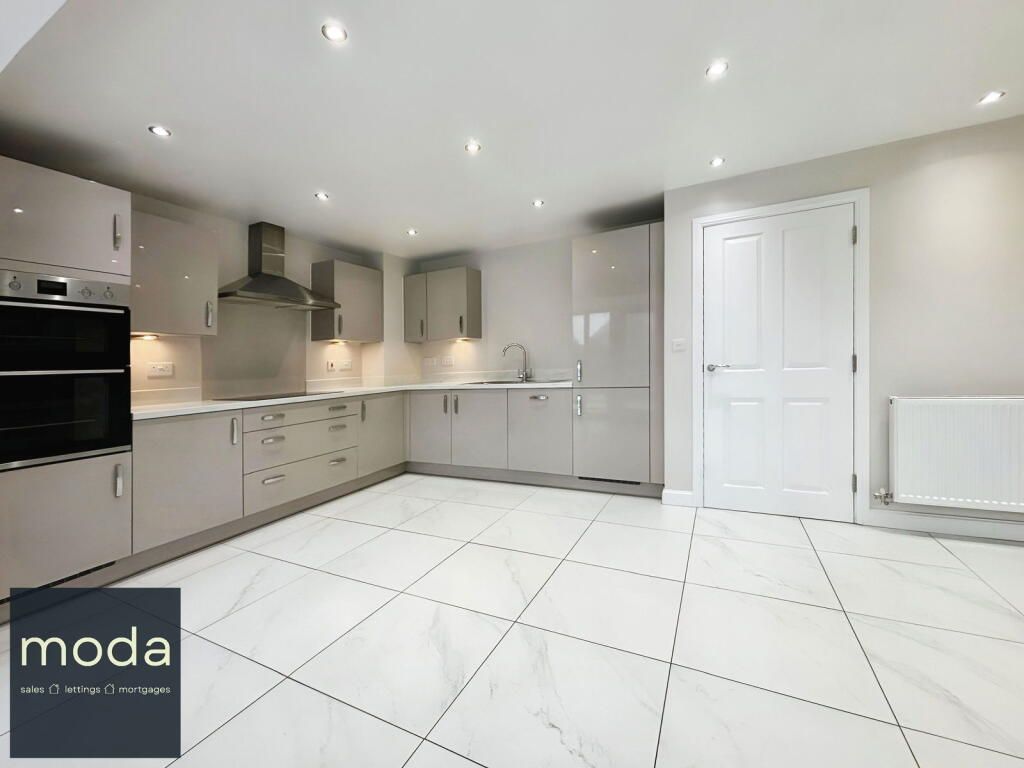 Modern, glossy gray kitchen with built-in appliances, white tiled floor, and a white door.