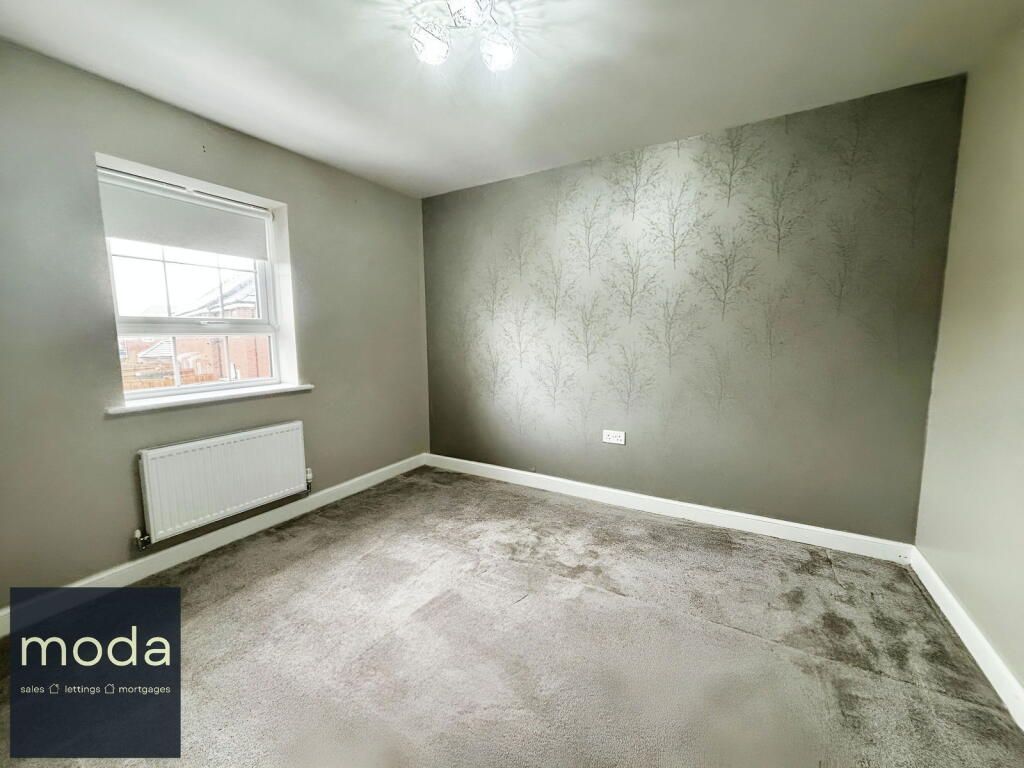 Empty bedroom with gray walls, window, radiator, and patterned carpet.