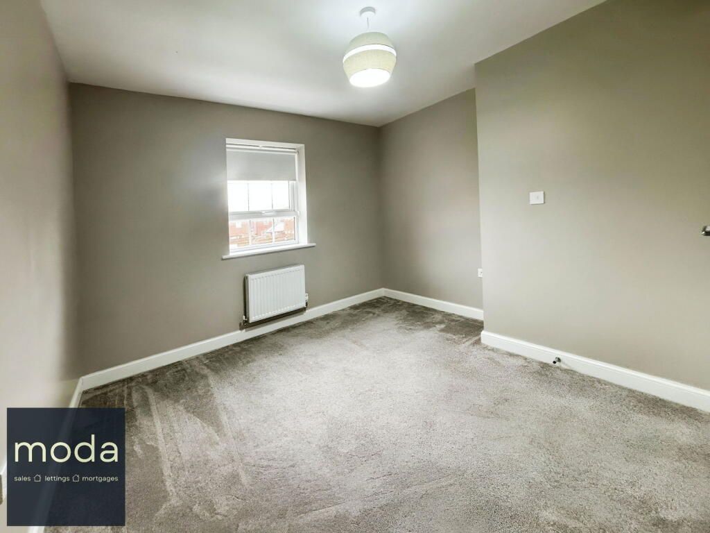 Empty room with gray walls, light-colored carpet, window, radiator, and a ceiling light.