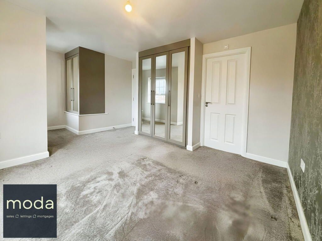 Bedroom with gray carpet, large mirrored wardrobe, and white door. Walls are neutral colors.