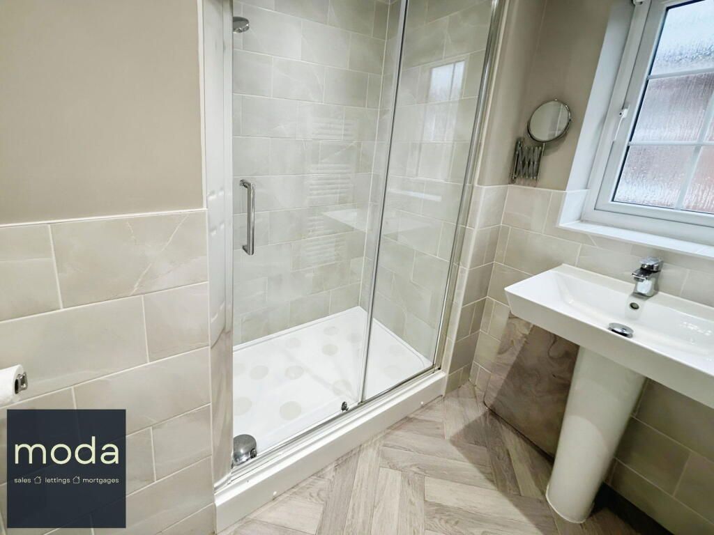 A modern bathroom with a glass shower, pedestal sink, and neutral-toned tiles.