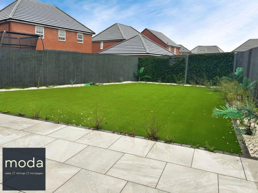 A backyard with a green lawn, gray patio, and a hedge.  Houses are in the background.