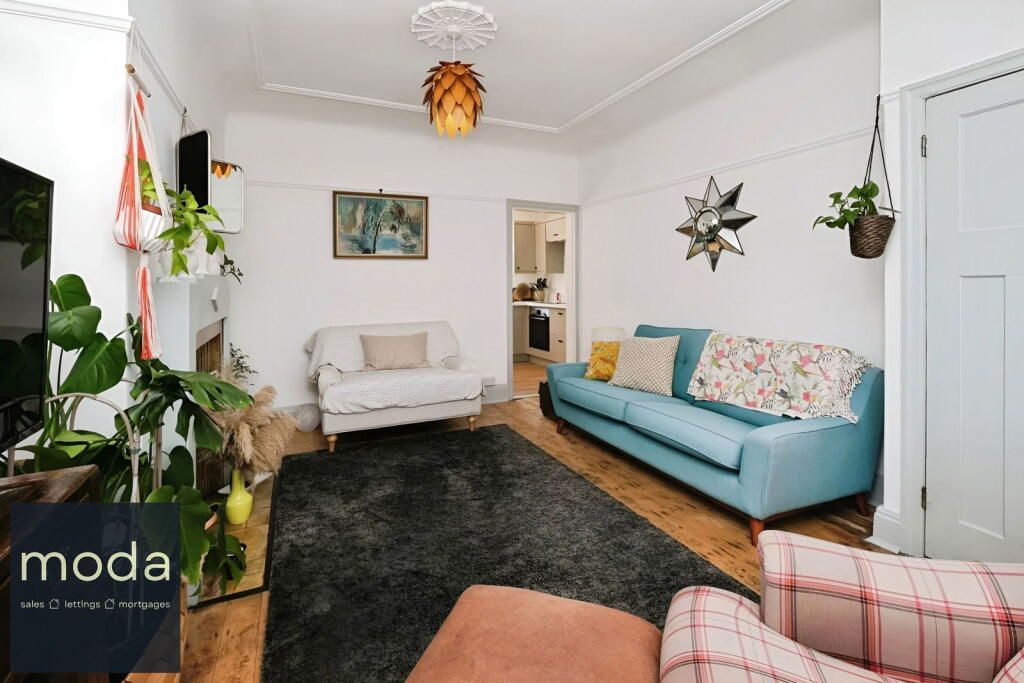 Living room with blue and cream sofas, rug, plants, and doorway to kitchen.