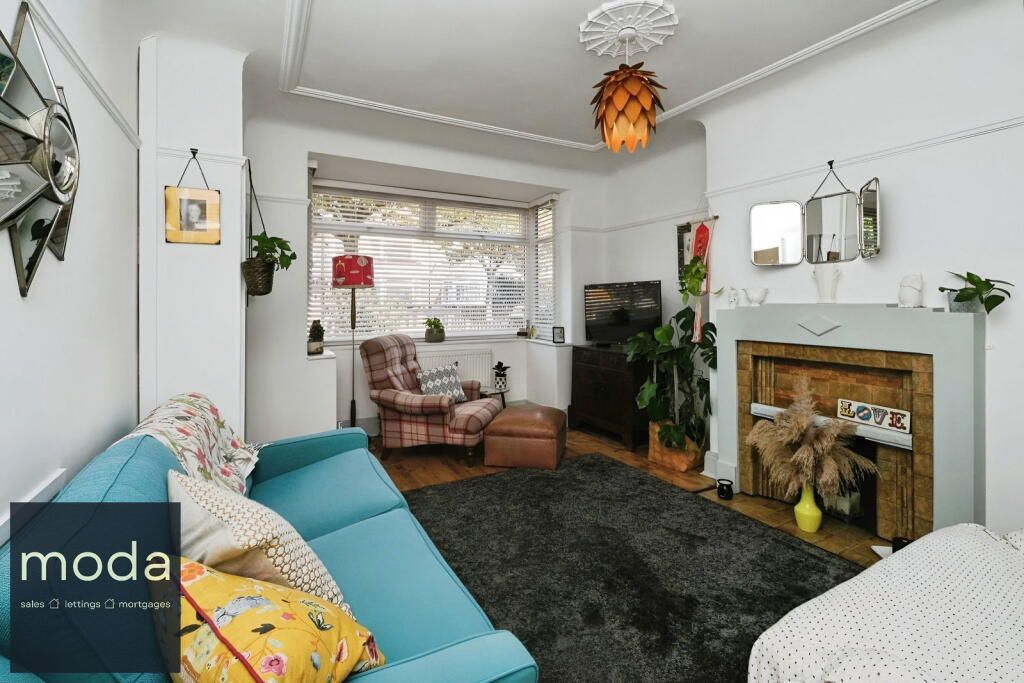 Living room with teal sofa, fireplace, and rug; featuring bay window, chair, and hanging decor.