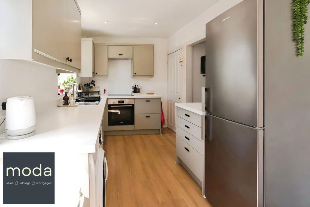 Modern kitchen with light cabinets, stainless steel fridge, and wood-look flooring.
