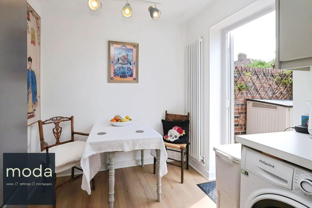 Kitchen with small table, chairs, open doorway to small outdoor area; white walls, light flooring.