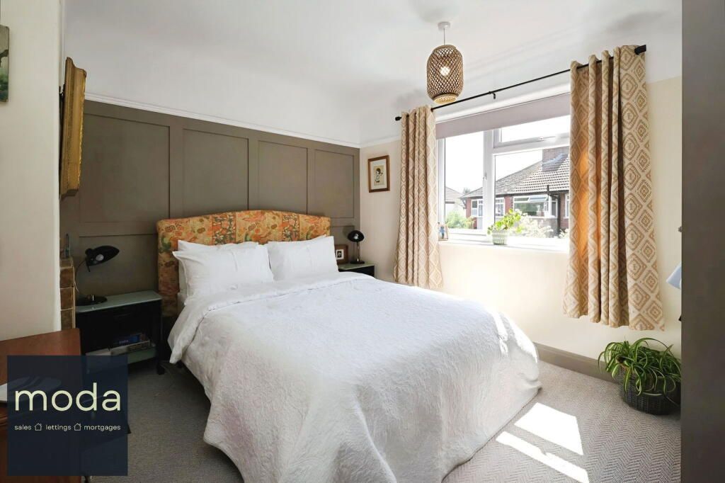 Bedroom with a double bed, brown panel wall, window with curtains, and a plant.
