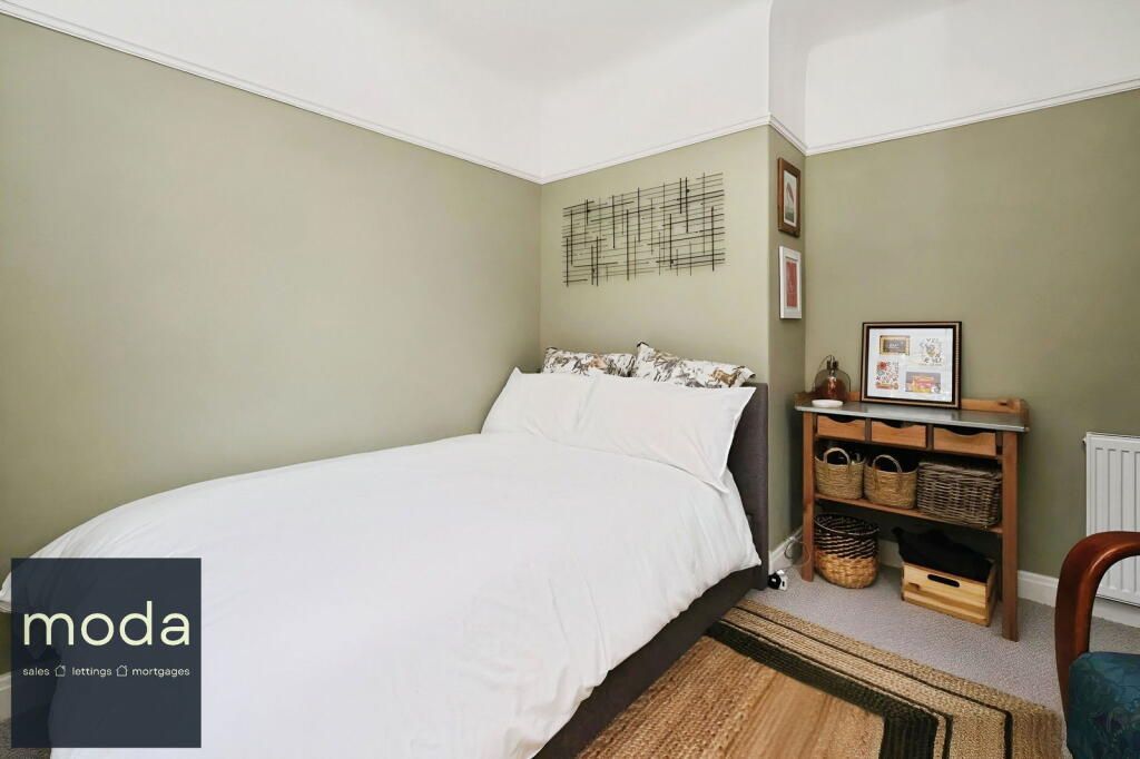 Bedroom with green walls, white bedding, artwork above bed, and a small table.