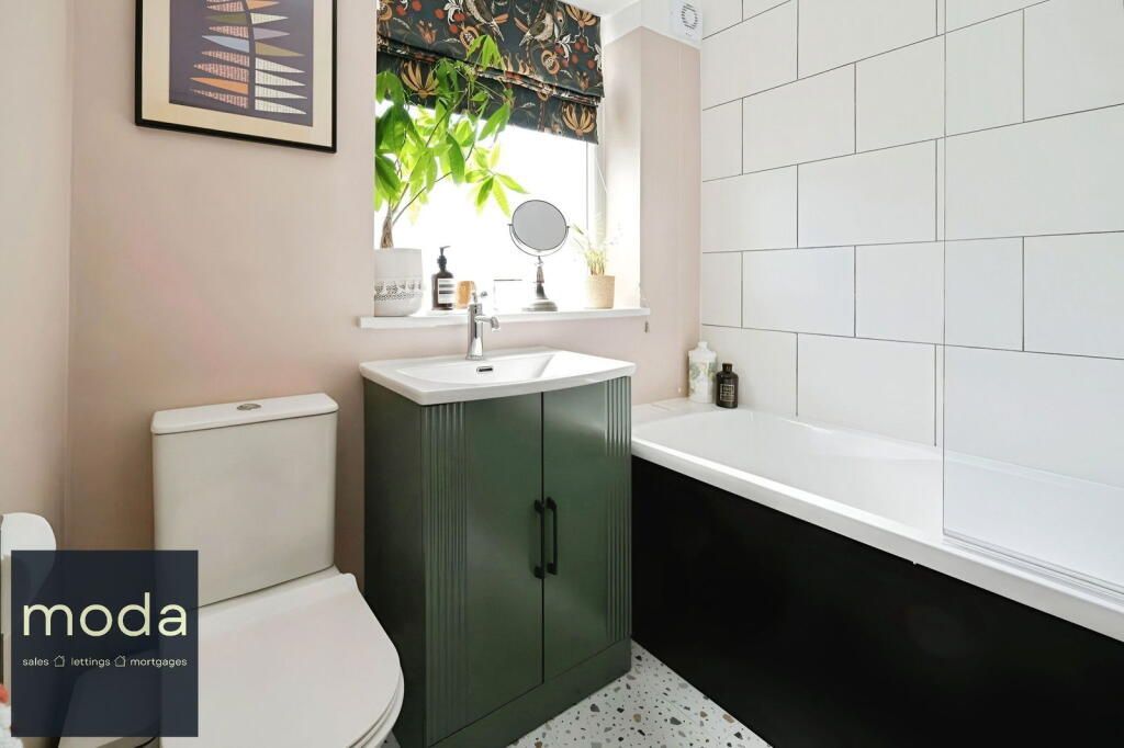 Bathroom with a green vanity, white toilet, white tub, and pink walls.