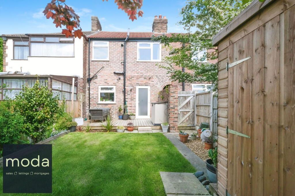 Backyard view of a brick house with a grassy lawn, garden path, and wooden shed.