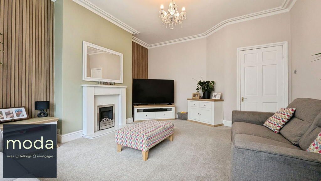 Living room with fireplace, TV, sofa, and ottoman; neutral tones, chandelier.