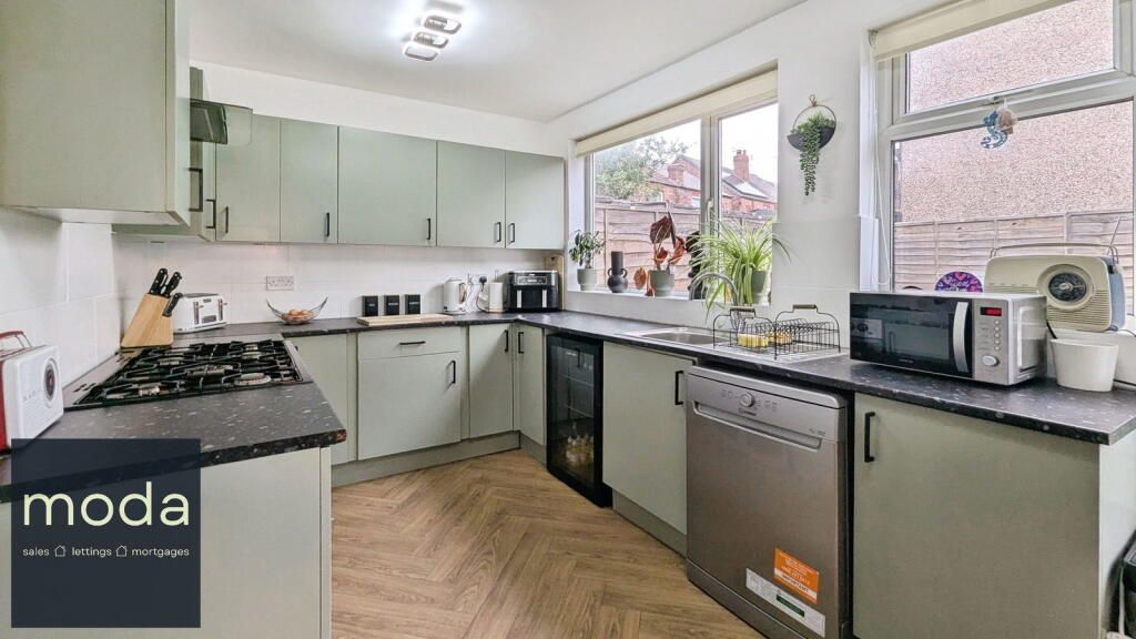 Kitchen with light green cabinets, black countertops, stainless steel appliances, and windows.