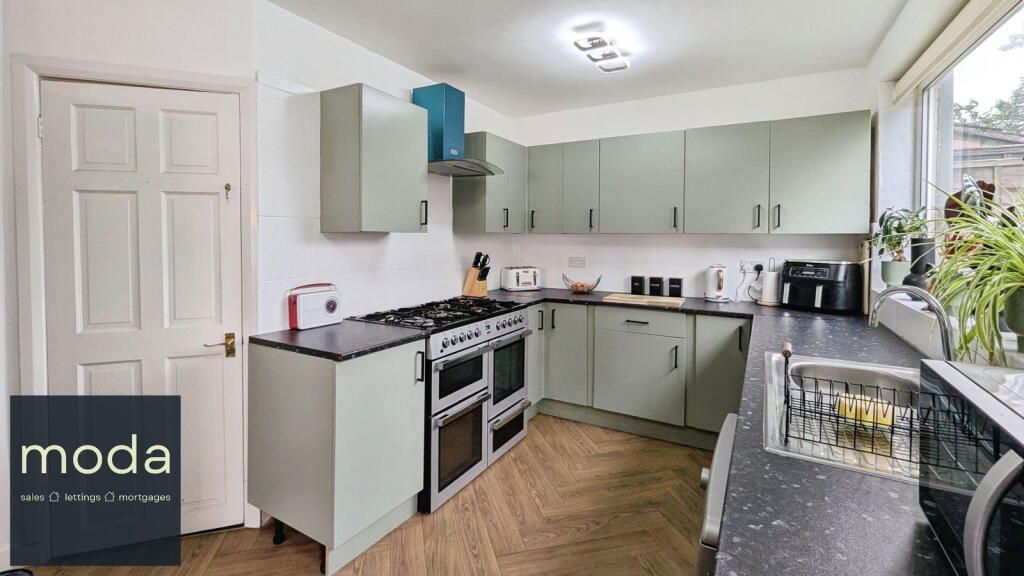 Kitchen with sage green cabinets, black countertops, and a large gas range.