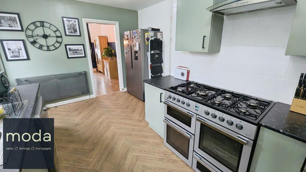 A kitchen with mint green cabinets, stainless steel appliances, and light wood flooring.