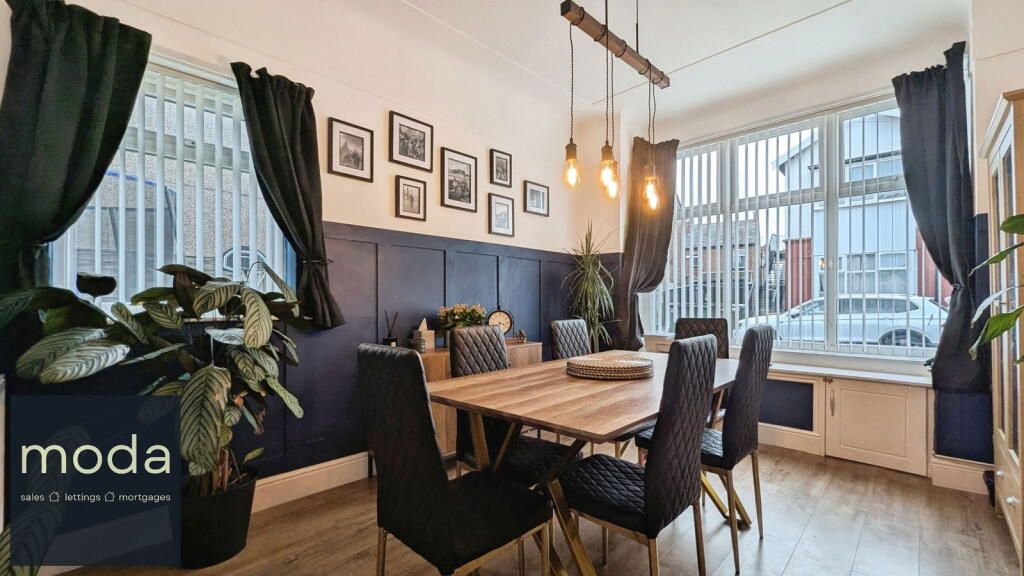 Dining room with a wooden table and six black chairs. Navy panelled wall, artwork, and dark curtains.