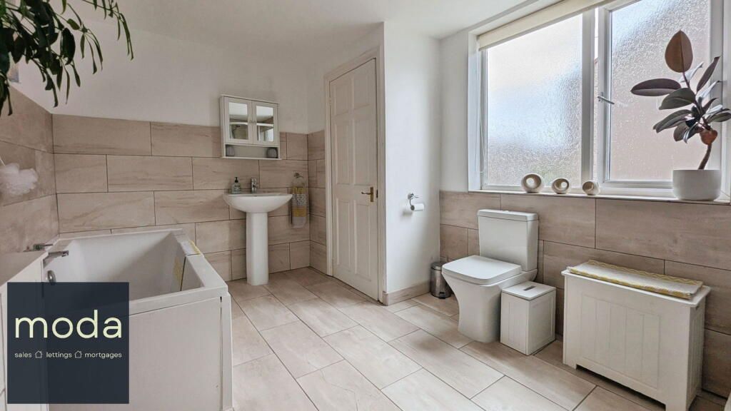 Bathroom with light-colored tiling, a white bathtub, toilet, and sink.  A window lets in light.