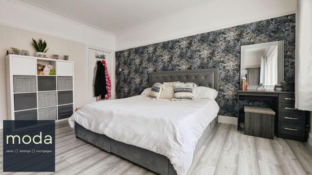 Bedroom with gray patterned wallpaper, bed, vanity, and storage unit.