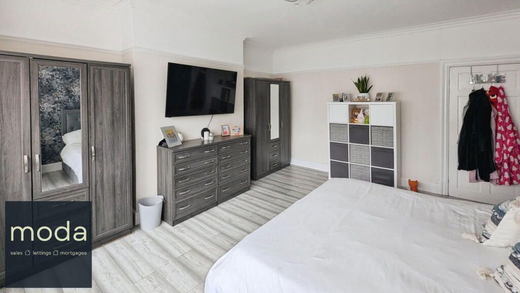 Bedroom with gray furniture, a TV, and a white bed. Clothing hangs on the door.