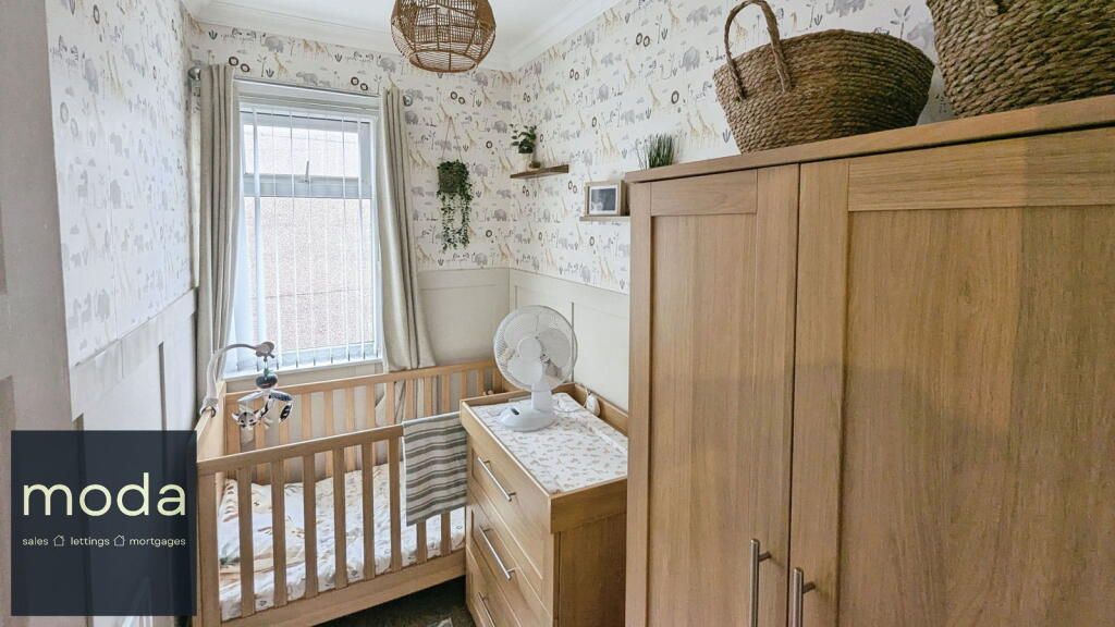 A nursery with light wood furniture and floral wallpaper. A crib, dresser, and wardrobe are visible.