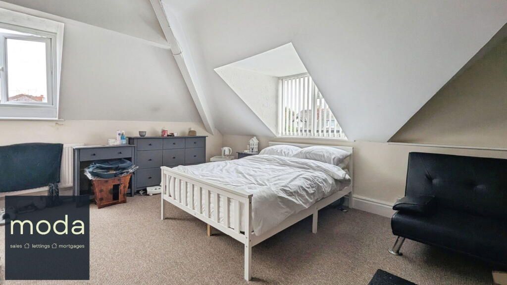 Bedroom with bed, dresser, chairs, and window in a slanted-ceilinged room.