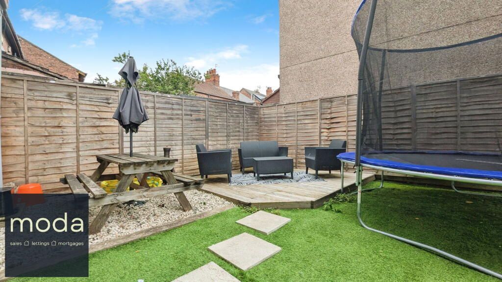 Backyard with wooden fence, seating area, picnic table, trampoline, and green grass.