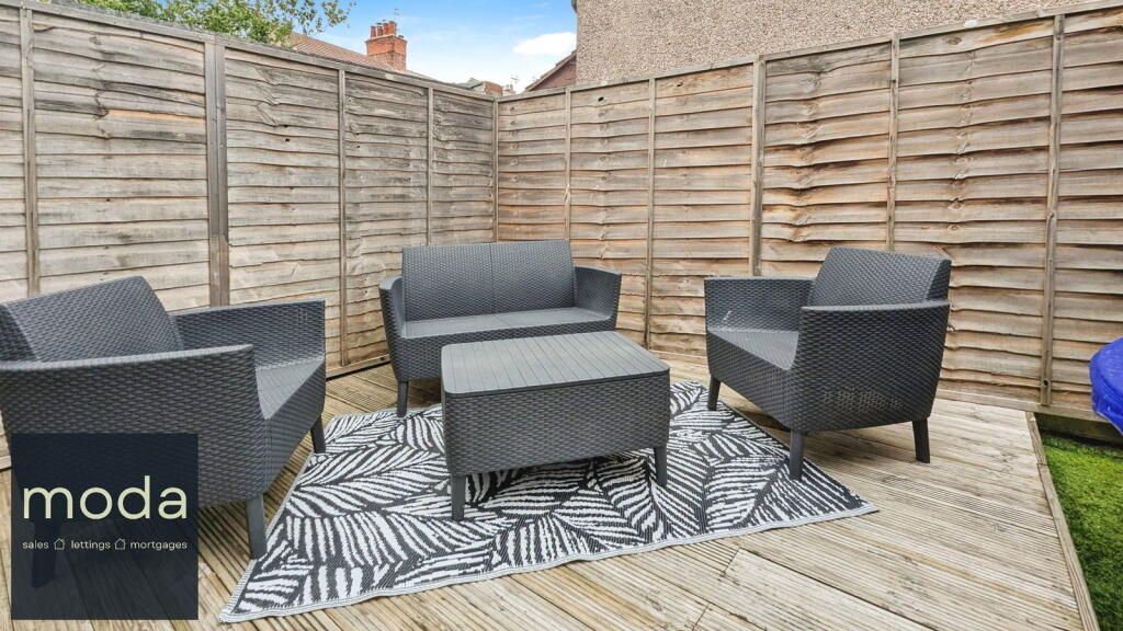 Outdoor patio with gray wicker furniture on a rug, surrounded by wooden fence.