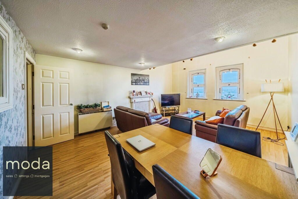 Spacious living area with dining table, sofas, fireplace, and windows. Natural light floods the room.