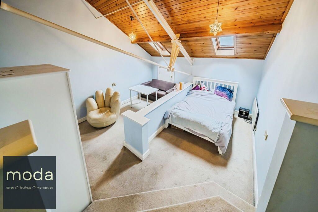 Bedroom with sloped wooden ceiling, bed, armchair, and desk.
